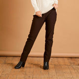 Person wearing brown pants and a white sweater on a wooden floor with a beige wall background