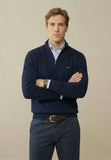 Man wearing a navy sweater over a light blue shirt with a beige background