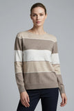 A woman modeling a CLAUDIA C beige, brown, and white striped knit sweater with textured horizontal bands and small heart motifs, paired with dark navy pants, against a solid gray studio background.