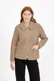 A woman modeling a MUDFLOWER taupe-brown sherpa fleece jacket with a front zipper, collar, and patch pockets, paired with black pants against a plain white studio background.