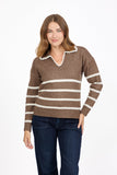 A woman modeling a MUDFLOWER brown knit sweater with horizontal cream stripes and a scalloped V-neck collar, paired with dark blue jeans, against a plain white background.